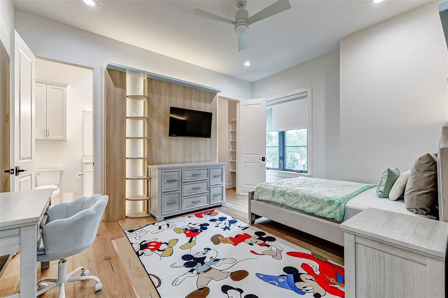 Bedroom number 4. This bright bedroom features an en suite bathroom, a large walk-in closet, a built-in entertainment center, custom LED lighting, and a cozy study area. It includes a bed, dresser, and a colorful rug.