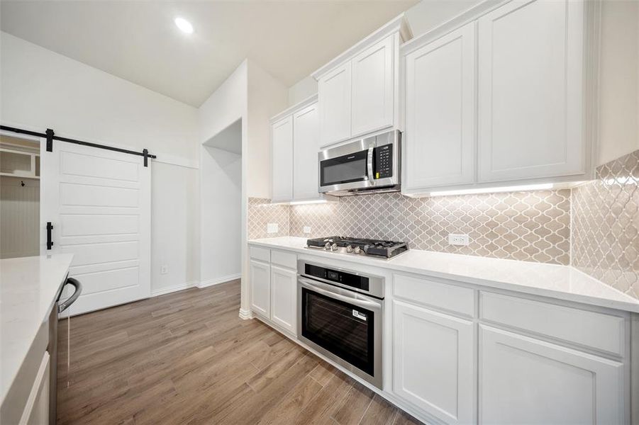 Kitchen featuring appliances with stainless steel finishes, white cabinetry, light wood finished floors, and decorative backsplash