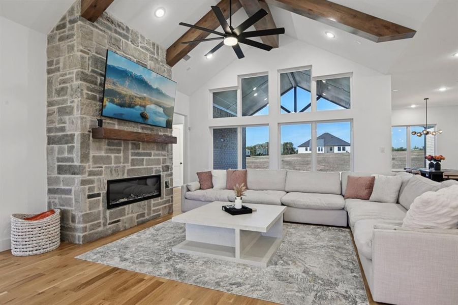 Living area featuring beam ceiling, light wood-style flooring, a fireplace, healthy amount of natural light, and a ceiling fan Living area featuring beam ceiling, light wood-style flooring, a fireplace, healthy amount of natural light, and a ceiling fan