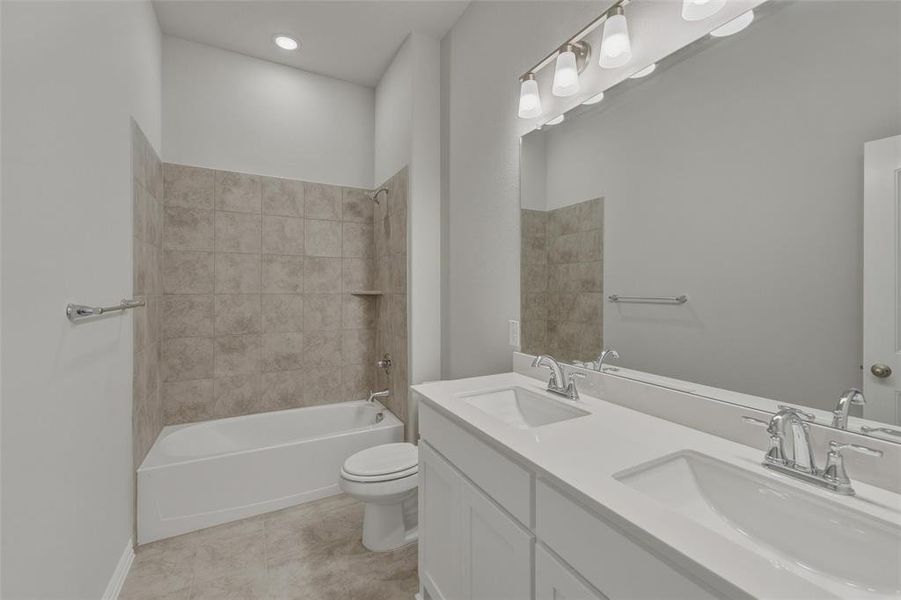 Bathroom featuring a dual-sink vanity with white countertops, a large vanity mirror, and a combination tub/shower with tiled surround and built-in shelving Bathroom featuring a dual-sink vanity with white countertops, a large vanity mirror, and a combination tub/shower with tiled surround and built-in shelving