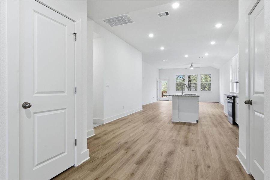 Kitchen featuring a center island with sink, vaulted ceiling, white cabinetry, light wood-style flooring, and recessed lighting