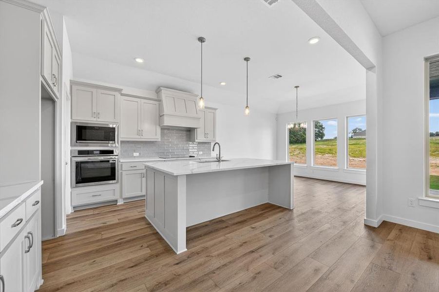 Modern kitchen with wood-finish flooring, light gray cabinetry, stainless steel built-in appliances, a quartz-finish island, and pendant lighting