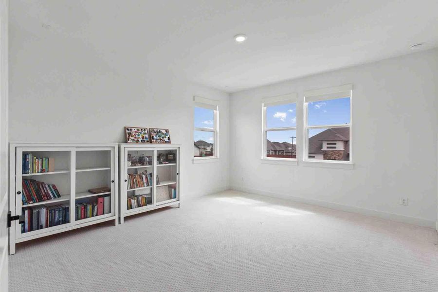 Bright room featuring three large windows, white walls, recessed lighting, and light-colored patterned carpeting