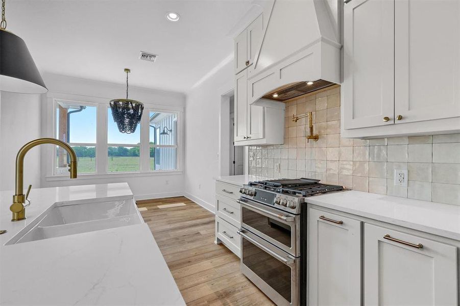 Kitchen with premium range hood, hanging light fixtures, white cabinets, double oven range, and light hardwood / wood-style flooring