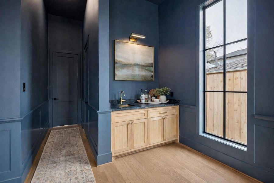 Built in beverage station tucked just off the office adds everyday convenience with custom light wood cabinetry, dark stone counters, and a brushed brass faucet. Oversized window and paneled walls continue the designer feel while creating a private coffee bar or cocktail setup within the workspace. *Virtually Staged*