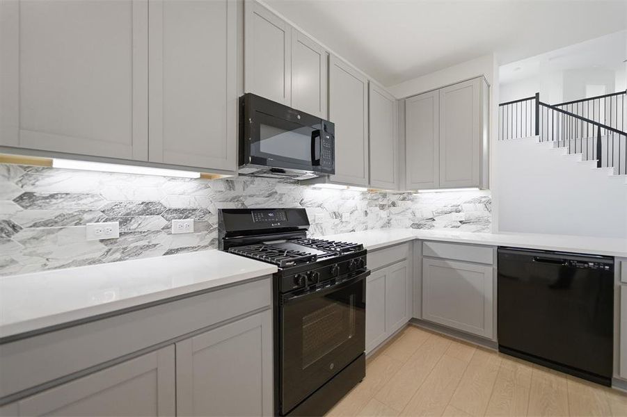 Kitchen featuring black appliances, gray cabinets, decorative backsplash, light wood-style flooring, and light stone counters