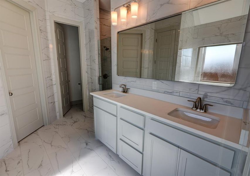 Bathroom featuring light marble finish floors, tile walls, and double vanity Bathroom featuring light marble finish floors, tile walls, and double vanity
