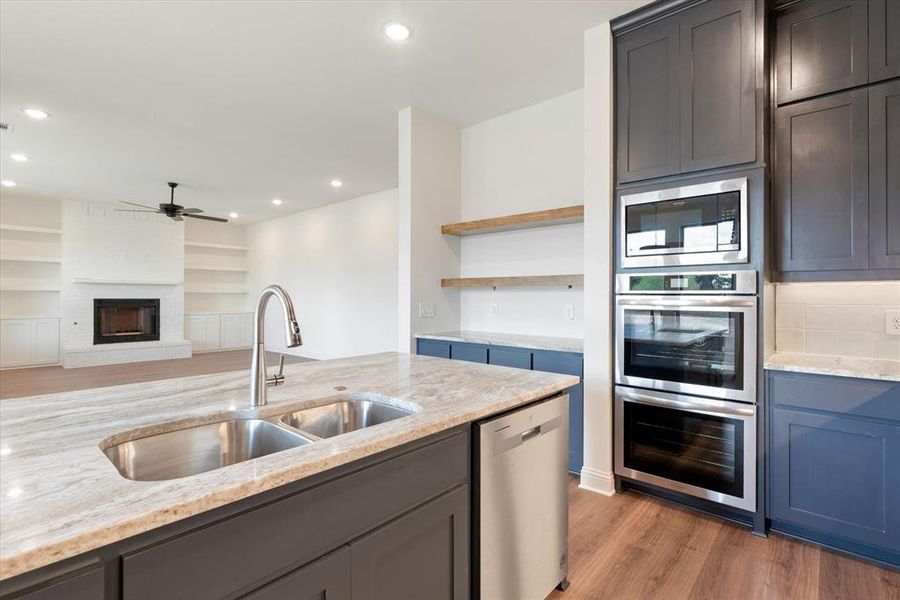 Kitchen with a fireplace, light wood-type flooring, light stone counters, stainless steel appliances, and sink