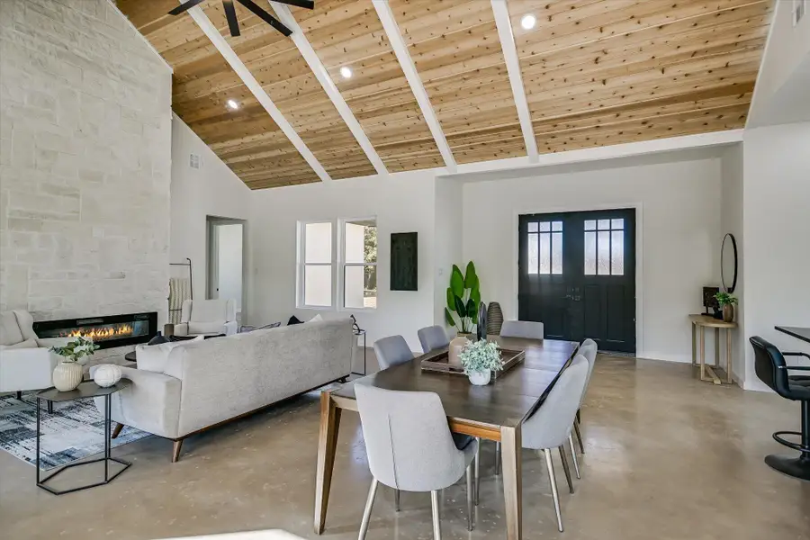 Dining area with high vaulted ceiling, a wooden ceiling with exposed beams, a fireplace, concrete floors, and recessed lighting