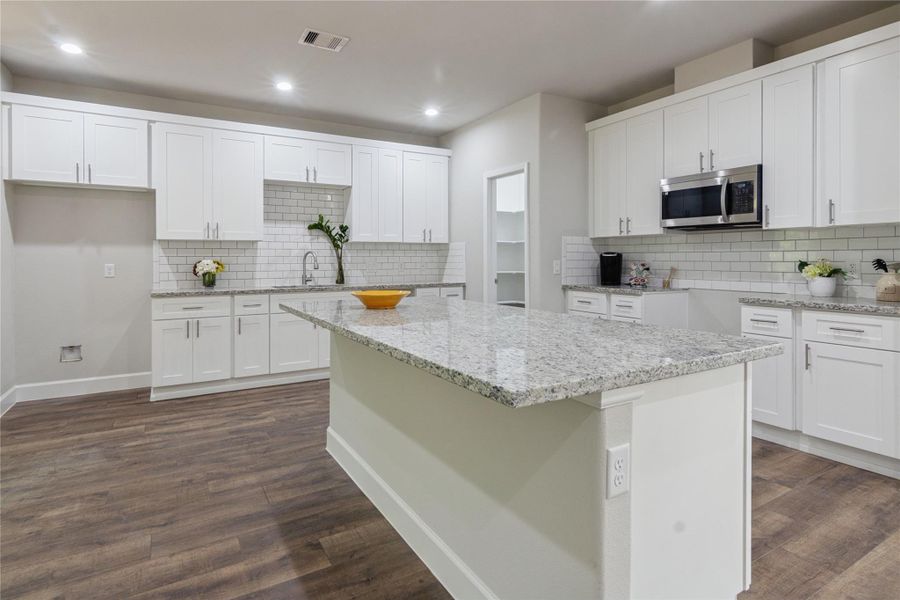 A modern kitchen featuring a spacious granite island, stainless steel microwave, and elegant subway tile backsplash.