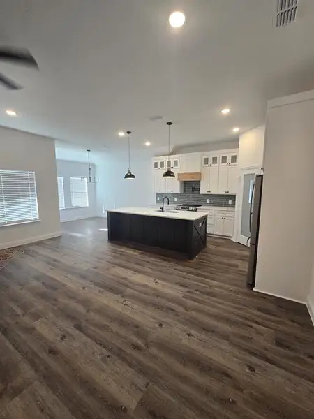 Kitchen featuring glass insert cabinets, white cabinetry, pendant lighting, open floor plan, and a kitchen island with sink