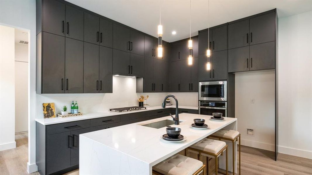 Kitchen with appliances with stainless steel finishes, light hardwood / wood-style floors, a kitchen island with sink, and sink