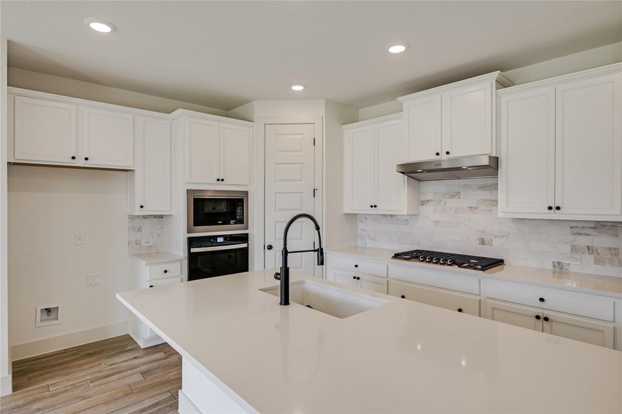 Kitchen with decorative backsplash, appliances with stainless steel finishes, recessed lighting, white cabinets, and light wood-style flooring