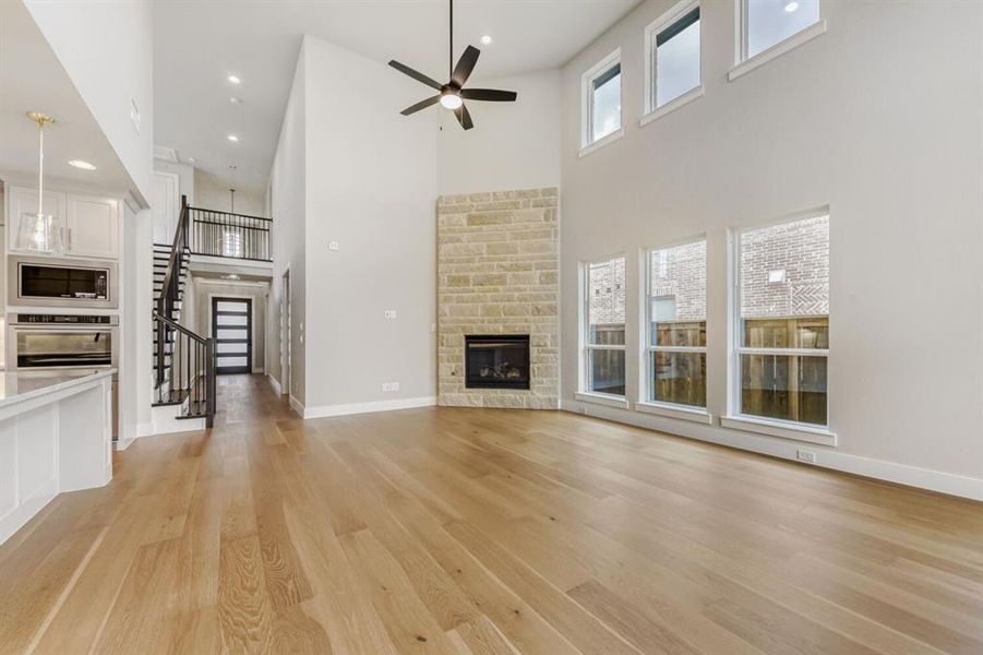 Unfurnished living room featuring a fireplace, ceiling fan, a high ceiling, light wood-style floors, and recessed lighting
