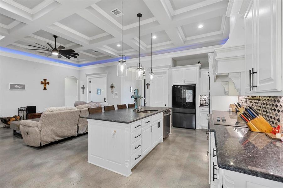 Kitchen featuring coffered ceiling, beamed ceiling, an island with sink, and black fridge