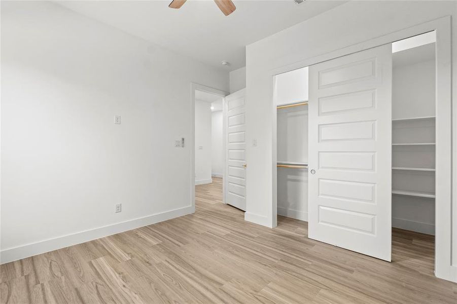 Unfurnished bedroom featuring light wood-style floors, ceiling fan, and a spacious closet