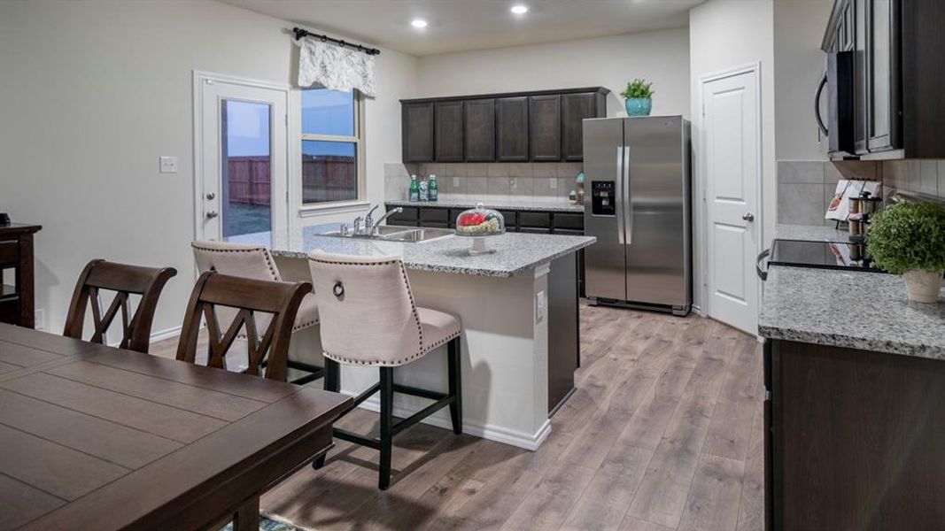 Kitchen featuring stainless steel appliances, a breakfast bar, light wood finished floors, light stone countertops, and dark wood finish cabinets
