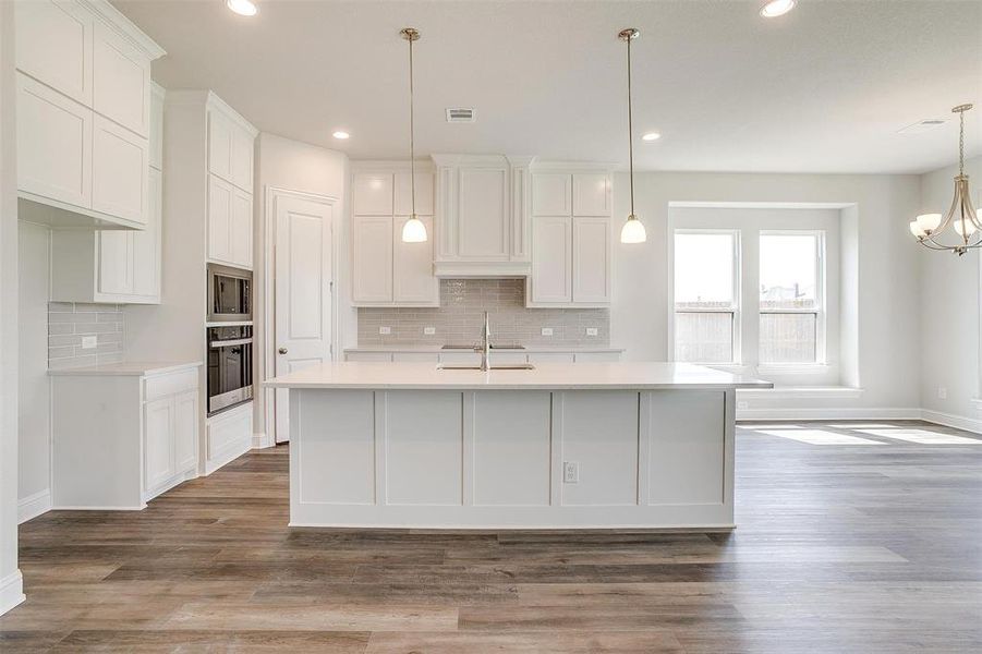 Kitchen with backsplash, decorative light fixtures, appliances with stainless steel finishes, hardwood / wood-style flooring, and a center island with sink