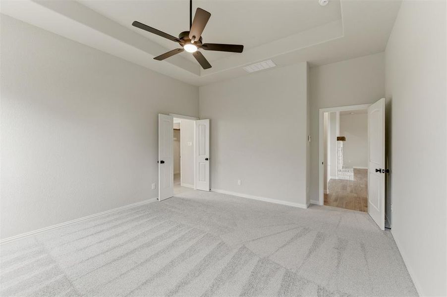Unfurnished bedroom featuring a tray ceiling, a ceiling fan, light carpet, and ensuite bathroom