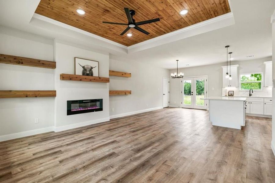 Open-concept living area featuring wood-finish flooring, a tray ceiling with wood paneling and recessed lighting, and a modern fireplace with integrated shelving