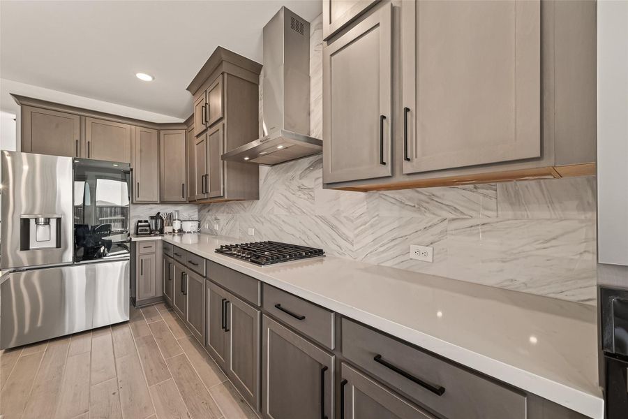 This modern kitchen features sleek stainless steel appliances, elegant wood cabinetry with ample storage, a stylish marble backsplash, and a spacious quartz countertop with a built-in gas cooktop.