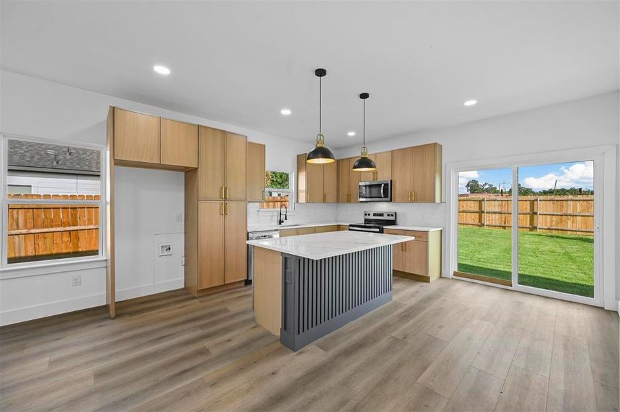 Kitchen featuring decorative light fixtures, backsplash, a center island, light wood-type flooring, and appliances with stainless steel finishes