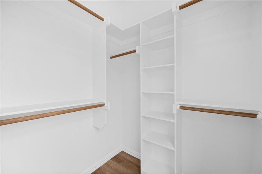 Spacious walk-in closet with built-in shelving and multiple hanging areas, offering ample storage and organization.