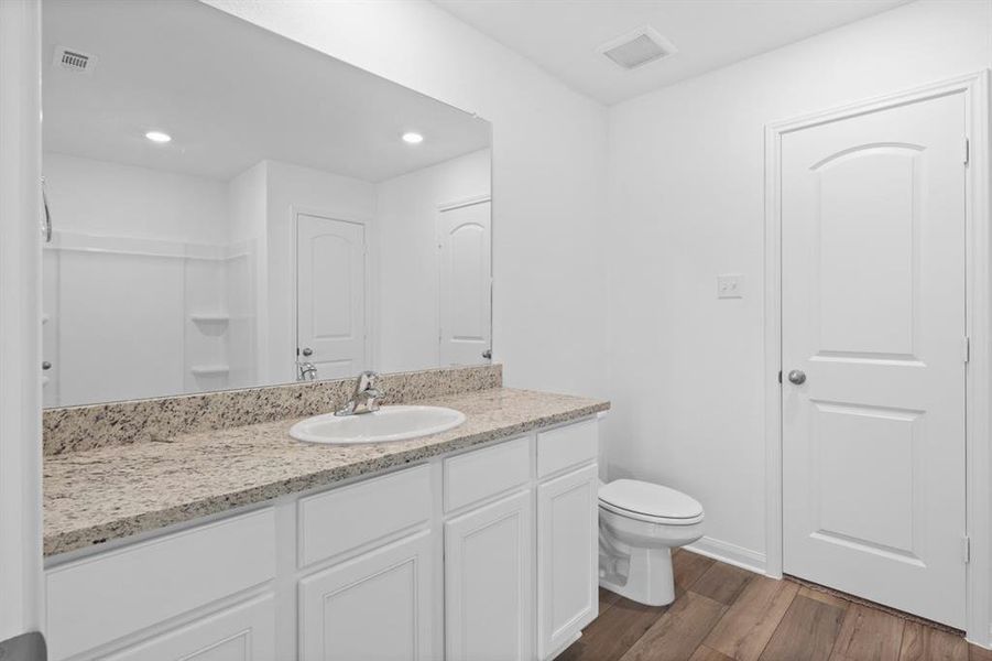 Primary bathroom includes granite counters, designer white cabinetry and luxury vinyl plank flooring.