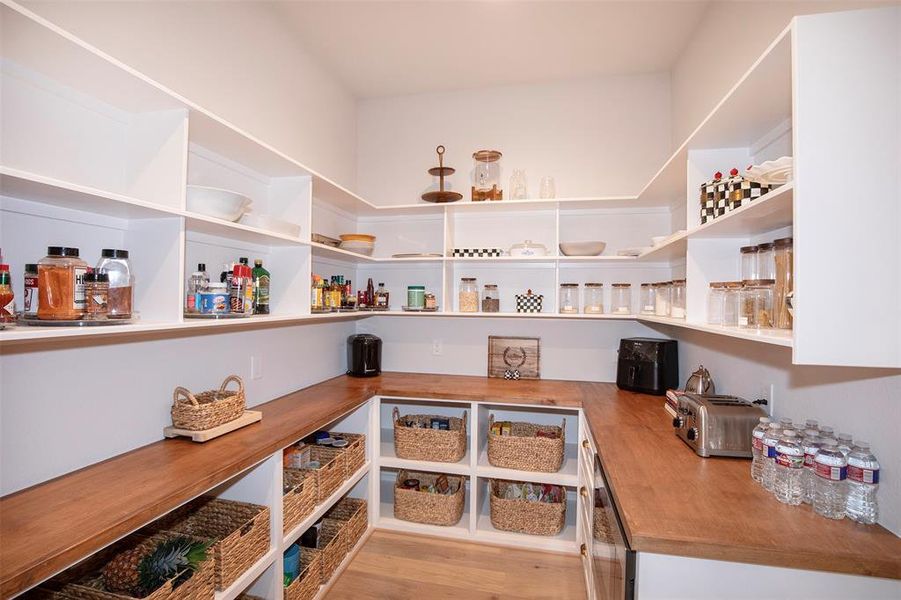 This spacious pantry features ample wooden countertops and open shelving, perfect for organizing kitchen essentials. It includes wicker baskets for storage and a variety of jars and containers, offering both functionality and style.