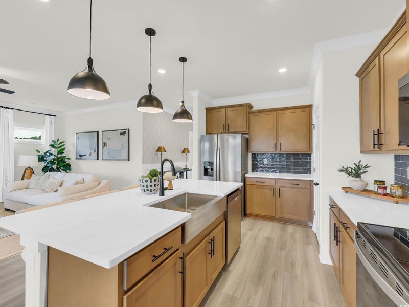 Kitchen featuring decorative backsplash, brown cabinetry, hanging light fixtures, light wood-style floors, and light stone countertops Kitchen featuring decorative backsplash, brown cabinetry, hanging light fixtures, light wood-style floors, and light stone countertops