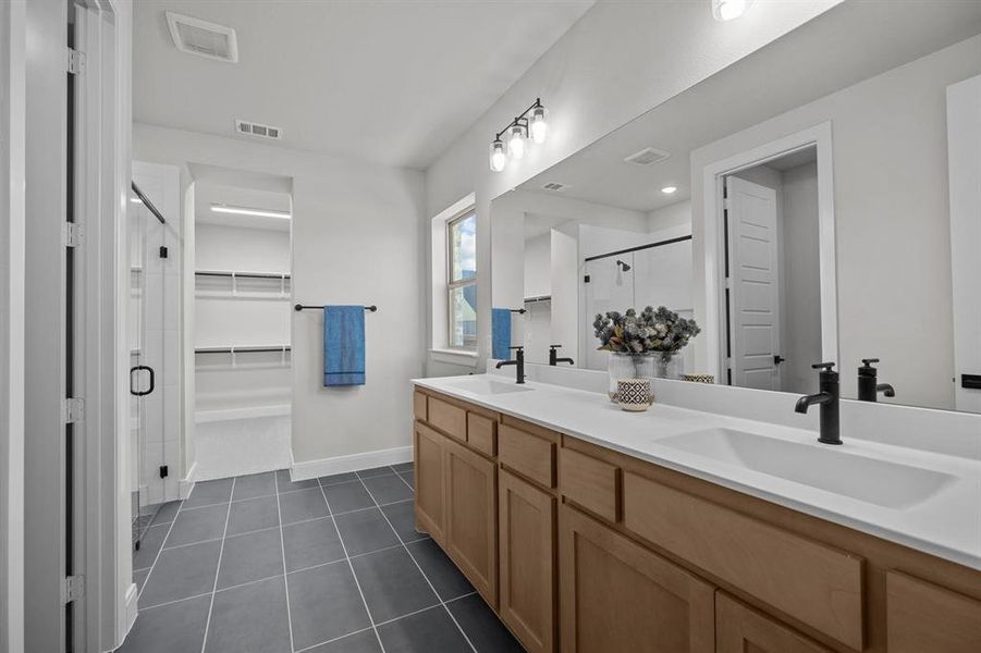 Spacious bathroom featuring a double vanity with light wood cabinetry, white countertops, and matte black fixtures Spacious bathroom featuring a double vanity with light wood cabinetry, white countertops, and matte black fixtures
