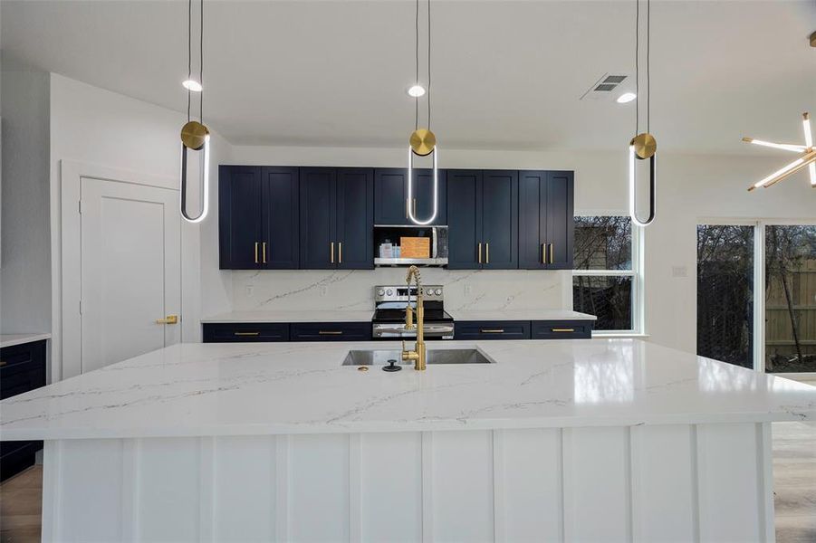 Kitchen with light stone counters, pendant lighting, and appliances with stainless steel finishes