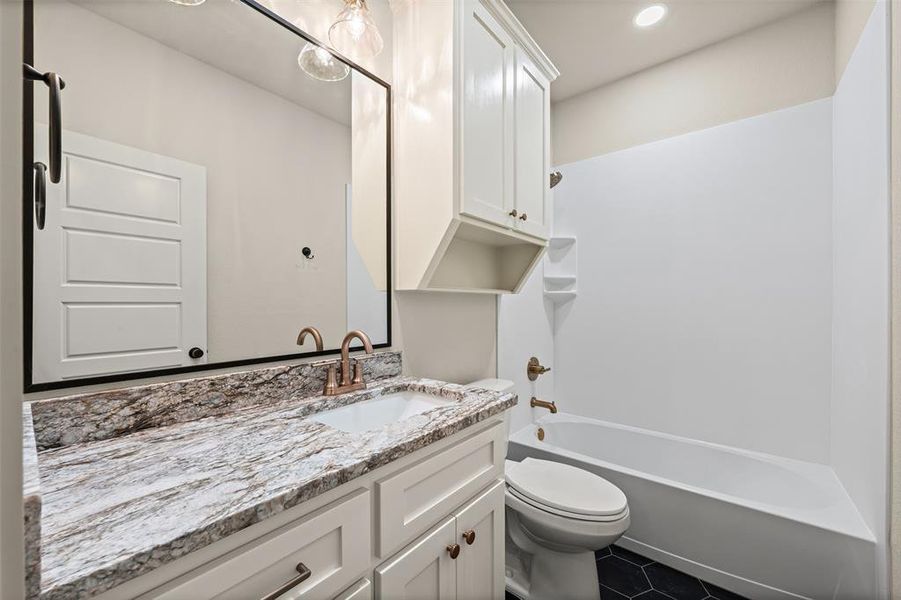 Bathroom with vanity, washtub / shower combination, and dark tile patterned floors
