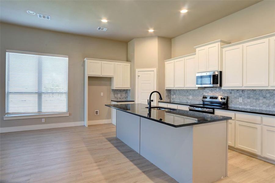 Kitchen featuring dark stone countertops, backsplash, a center island with sink, appliances with stainless steel finishes, and recessed lighting Kitchen featuring dark stone countertops, backsplash, a center island with sink, appliances with stainless steel finishes, and recessed lighting