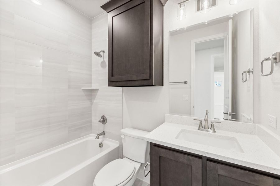 Bathroom with dark wood vanity, white quartz countertop, tub-shower combo, and white tile walls Bathroom with dark wood vanity, white quartz countertop, tub-shower combo, and white tile walls