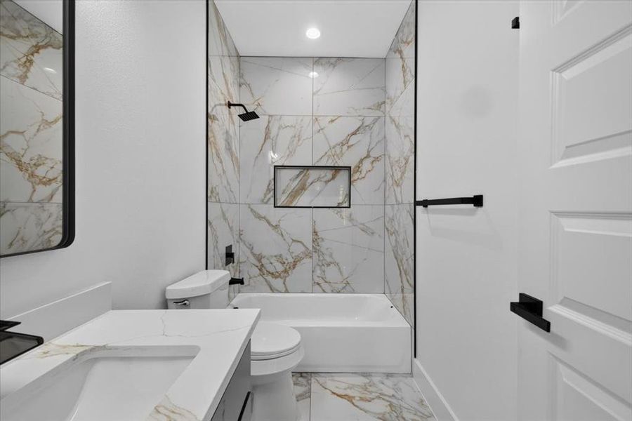 Modern bathroom featuring a bathtub with a shower, white and gold veined tile surround, and a recessed shower niche Modern bathroom featuring a bathtub with a shower, white and gold veined tile surround, and a recessed shower niche