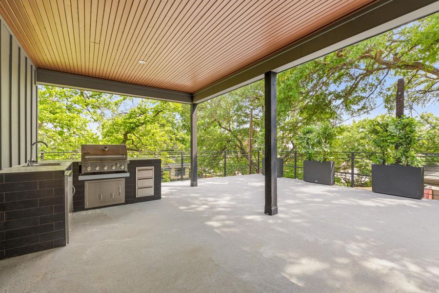 Expansive covered patio featuring a built-in outdoor kitchen with a stainless steel grill, sink, and cabinetry