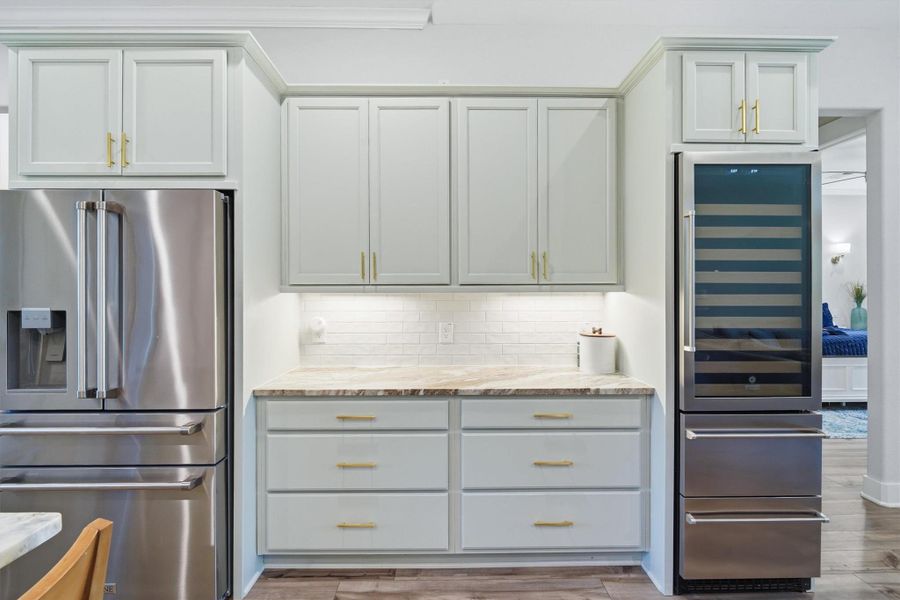 Popular shaker style cabinets with brushed brass hardware, pull out drawers accented by under cabinet lighting. Stainless steel wine refrigerator with beverage bins Popular shaker style cabinets with brushed brass hardware, pull out drawers accented by under cabinet lighting. Stainless steel wine refrigerator with beverage bins
