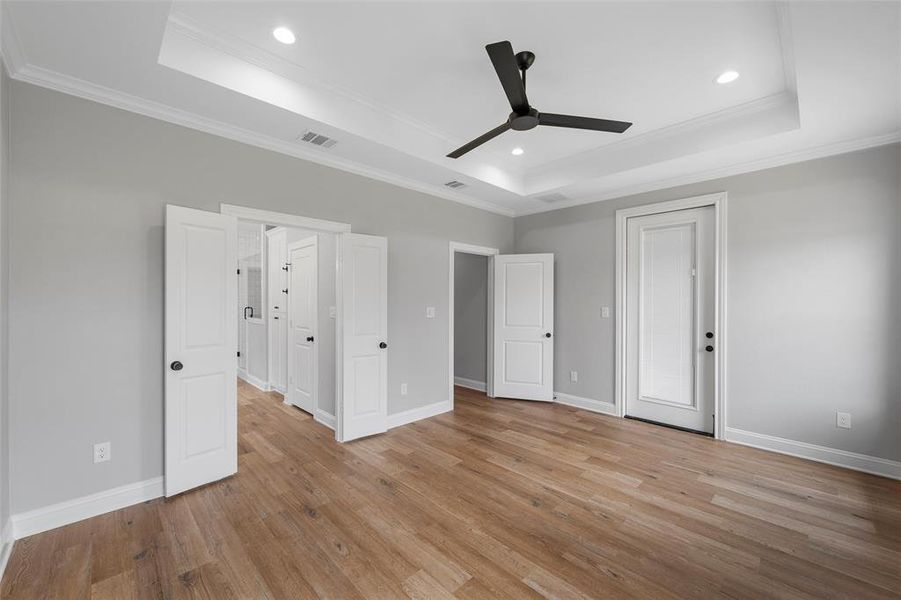 Unfurnished bedroom featuring a raised ceiling, light wood-type flooring, ornamental molding, recessed lighting, and a ceiling fan Unfurnished bedroom featuring a raised ceiling, light wood-type flooring, ornamental molding, recessed lighting, and a ceiling fan