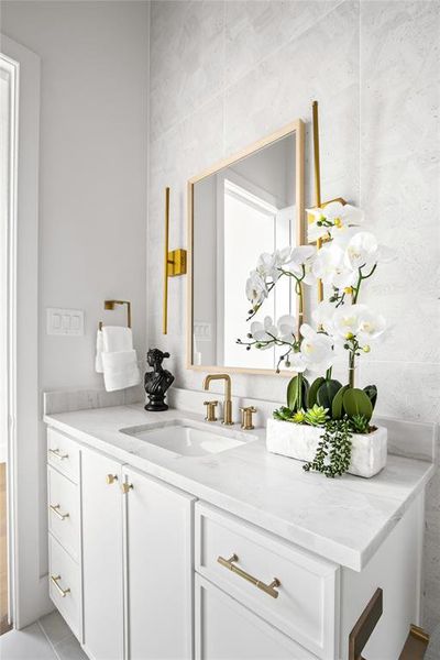 White vanity featuring a rectangular undermount sink, brass-finish faucet, and coordinating hardware