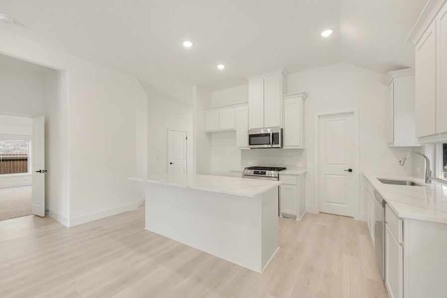 Open kitchen with white cabinets, center island, stainless steel appliances, and light hardwood floors Open kitchen with white cabinets, center island, stainless steel appliances, and light hardwood floors