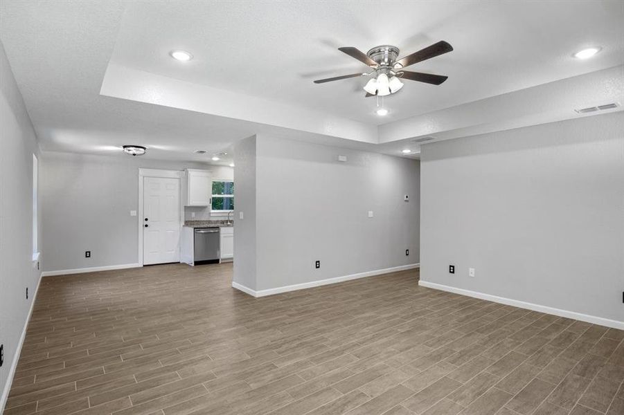 Unfurnished living room with a tray ceiling, ceiling fan, recessed lighting, and wood tiled floors Unfurnished living room with a tray ceiling, ceiling fan, recessed lighting, and wood tiled floors
