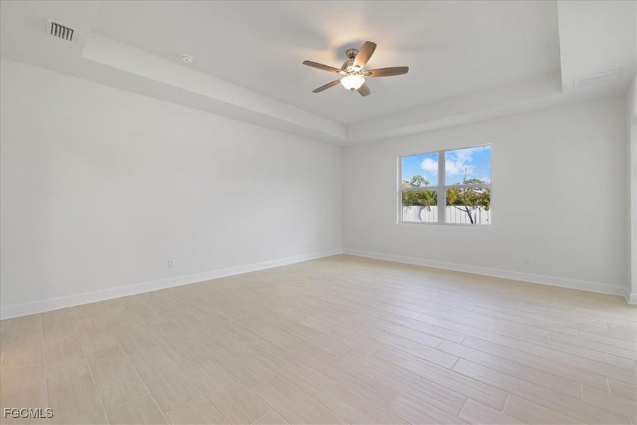 Empty room featuring a tray ceiling, a ceiling fan, and light wood-style floors Empty room featuring a tray ceiling, a ceiling fan, and light wood-style floors