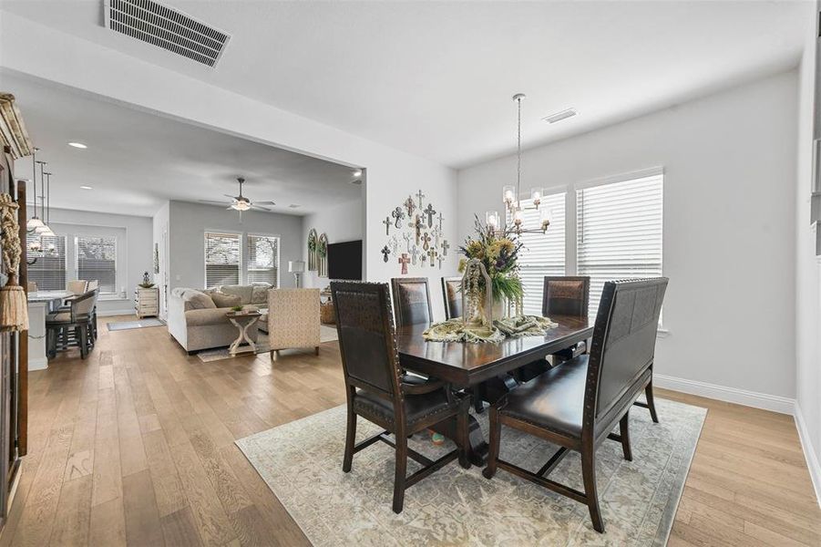 Dining room with light wood-type flooring and ceiling fan with notable chandelier