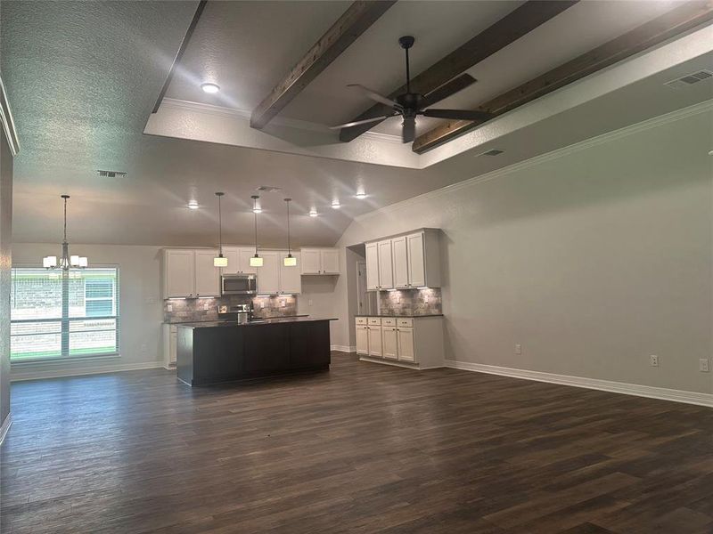 Unfurnished living room featuring ceiling fan, a chandelier, dark wood finished floors, and ornamental molding