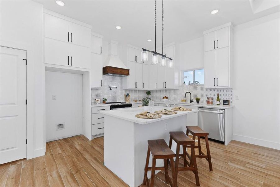 Kitchen featuring a kitchen breakfast bar, light wood-type flooring, decorative light fixtures, white cabinets, and recessed lighting