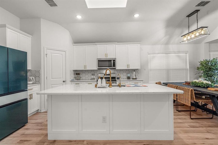 Kitchen with light hardwood / wood-style floors, white cabinetry, an island with sink, and appliances with stainless steel finishes