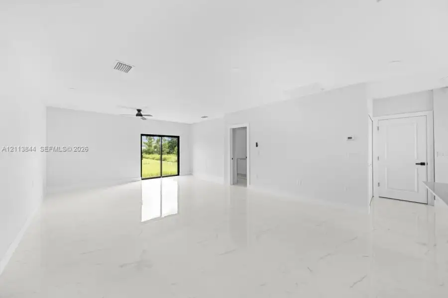 Open interior space featuring polished stone-finish tile flooring, recessed ceiling lighting, a matte black ceiling fan, and sliding glass doors Open interior space featuring polished stone-finish tile flooring, recessed ceiling lighting, a matte black ceiling fan, and sliding glass doors