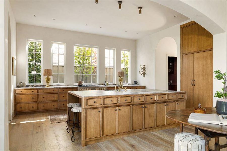 Kitchen featuring brown cabinetry, light countertops, light wood-type flooring, a center island with sink, and a breakfast bar area