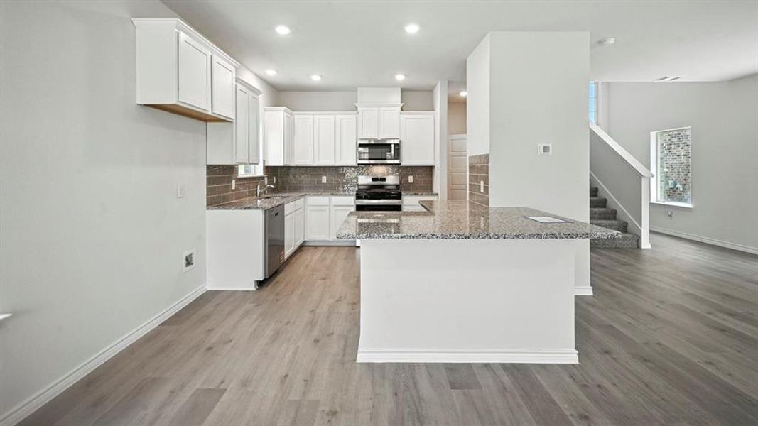 Kitchen with white cabinets, dark stone counters, backsplash, stainless steel appliances, and a peninsula
